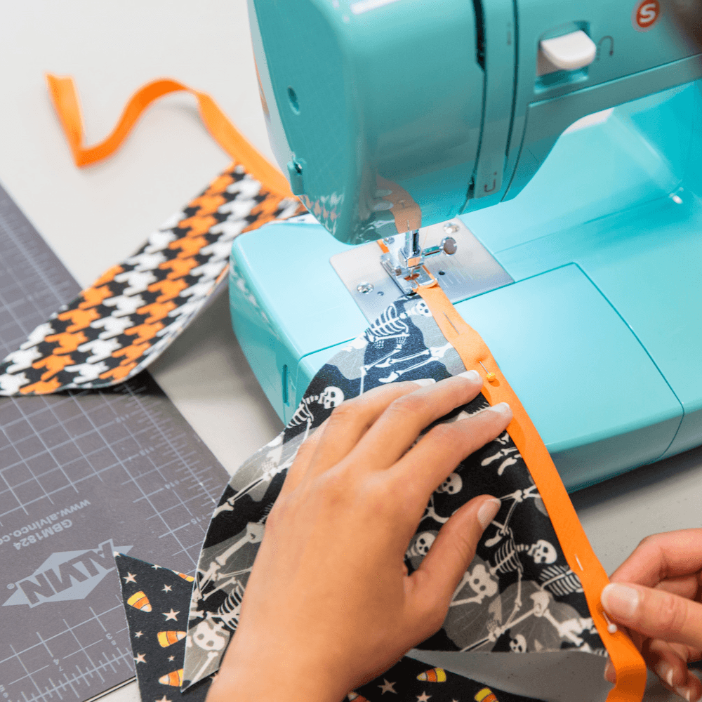 Hands feeding fabric bunting sewing project through a sewing machine